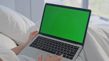 Eller sabahları evdeki bilgisayarda çalışıyor. Bilinmeyen kadın, beyaz yatakta yeşil ekran bilgisayar dokunmatik dokunmatik web sitesi kullanıyor. Parlak yatak odasında internetten okuyan kız öğrenci..