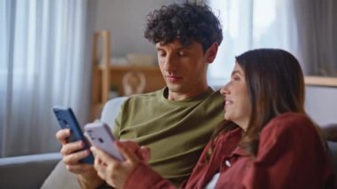 Çevrimiçi çift evde cep telefonlarını dinlendiren kanepeye bakıyor. Cep telefonunu izleyen gülen adam sosyal medyayı inceliyor. Genç aile oturma odasında akıllı telefon okuması yapıyor. 
