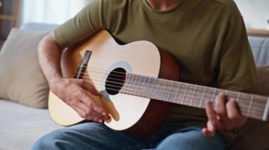 Gitarist elleri yakın planda şarkı provası yapıyor. Gülümseyen, kulaklıklı, gitar çalan, tellere dokunan profesyonel müzisyen. Rahatlamış adam oturma odasında müziğin tadını çıkarıyor. Hobi konsepti 
