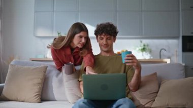 Modern oturma odasında dizüstü bilgisayar arayan çift. Rahat bir adam kanepede oturmuş bilgisayardan alışveriş yapan bir kadınla kahve içiyor. Mutlu genç ortaklar dairedeki e-ticaret mağazasında alışverişi tartışıyor. 