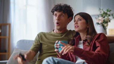 İki izleyici TV 'de rahat bir kanepede film izliyor. Gülümseyen çift evde televizyonla vakit geçiriyor. Harika bir çift parmak göstererek yumuşak koltukta eğlenceli eğlence programının tadını çıkarır. 