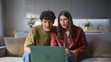 Gülen çift, apartmanın yakın çekimlerinde uzaktan iletişimin keyfini çıkarıyor. Mutlu ruh eşleri evde otururken internette sohbet ediyorlar. Kanepede bilgisayar kamerasına veda eden gülümseyen bir çift.