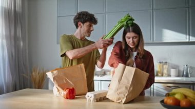 Marketten paketleri çıkaran genç bir çift ev mutfağını kapatıyor. Mutlu aşıklar kağıt eko poşetinden organik yiyecek alırken eğleniyorlar. Alışveriş sonrası tatlı bir çift alışverişi. 