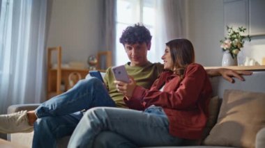 Genç çift rahat bir odada akıllı telefonları yakından izliyor. Sevgilisiyle bağ kuran kız rahat koltukta komik videoların keyfini çıkarıyor. Rahat kız evde eğlenen bir adamla dinleniyor. Aile hafta sonu konsepti 