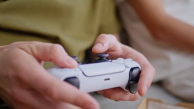 Çocuk parmakları video oyunu oynuyor kanepe oturma odasında yakın plan. İsimsiz bir adam kız arkadaşının konsoluyla rekabete odaklanmış. Bilinmeyen oyuncu ergen hafta sonu sabah oyun hobisinin tadını çıkarıyor 