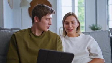 Mutlu ruh eşleri konuşma sekmesi. Oturma odasında yakın çekim. Gülümseyen genç çiftler birbirleriyle iletişim kuruyorlar ve bilgisayarlarına bakıyorlar. Gülen gençlerin videosu uzaktaki konuşmada iyi haberler veriyor.
