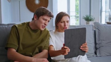 İnternette konuşan iki arkadaş bilgisayarın başında oturmuş kanepeyi kapatıyorlar. Gülümseyen genç çift kanepedeki tablet web kamerasını arıyor. Mutlu gençler apartmanda uzaktan iletişimin keyfini çıkarıyorlar.