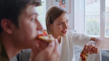 En iyi arkadaşlar hafta sonunu rahat bir kanepede pizza yiyerek geçiriyorlar. Gülümseyen mutlu kadın oturma odasında erkek arkadaşıyla konuşuyor. Rahatlamış ruh eşleri televizyon seyrediyor ellerinde yerel atmosferde kesikler var.