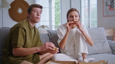 Hafta sonu çifti TV karşısında oturup pizza yiyor. Mutlu aşıklar programı izlerken fast food tatma programı izliyorlar. Rahat erkek arkadaş elinde dilimlerle konuşuyor. Gençler odada dinleniyor.