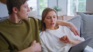 Genç sevgililer, aydınlık oturma odasında, tablet üzerinde internette sörf yapıyorlar. Sevimli gençler rahat evlerinde bilgisayardan fotoğraf izliyorlar. Kapalı mekanda dijital cihaz kullanan çekici çift.