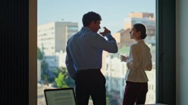 Ofis arkadaşları panoramik bina penceresinde kahveyi paylaşıyorlar. Rahatlamış iş arkadaşları şehir manzarasının tadını çıkarıyorlar birlikte aromatik içecekler içiyorlar. Zarif bir kadın iş yerinde dost canlısı bir adamla konuşuyor..