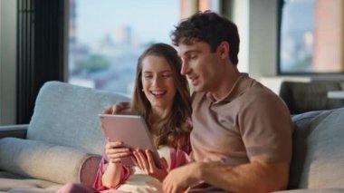 Mutlu çift tablet izleyip sıcak bir evde birlikte oturuyorlar. Rahat erkek ve kadın rahat oturma odasında dijital etkileşimden zevk alıyor. Sevgi dolu çiftler online alışverişleri koltukta seçiyor..