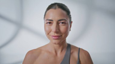 Beyaz duvar arka planında poz veren kadın yogi portresi. Huzurlu, çekici bir kadın, sükuneti hissediyor. Kapalı mekanlara yakından bakıyor. Spor giyim kuşağında rahat yoga kızı doğruca geniş stüdyoya bakıyor.