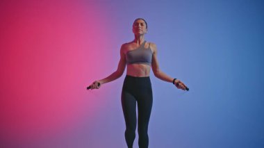 Neon spor kulübüne atlayan ciddi bir fitness kadını. İp atlama kullanan genç bayan sporcu boş odada motive olmuş hissediyor. Güçlü bayan eğitimini tek başına belirlemek. Etkin yaşam tarzı kavramı 