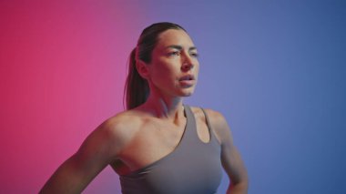 Yorgun bir kadın neon ışıkta dikiliyor. Yorgun bayan sporcu kameraya bakıyor, kardiyo çalışması portresinde dinleniyor. Sporcu kadın fiziksel egzersiz yapıyor. Sıkı çalışma dayanıklılığı 
