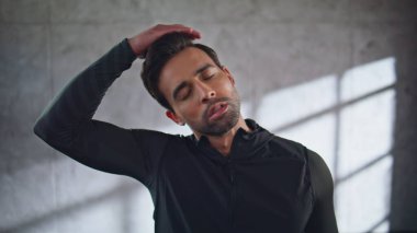 Spor salonundaki adam stüdyo resminde boynu gererek ısınıyor. Spor giyim sektöründeki atletik adam sıkı çalışmaya hazırlanıyor. Sporcu sabah rutininin tadını çıkarıyor. Esmer, içeride egzersiz yapıyor. 