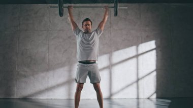Spor kulübünde halter kaldıran güçlü bir adam. Ağırlık egzersizi ile profesyonel vücut geliştirme eğitimi. Güçlü bir sporcu ağır nefes alıyor ve ekipmanları yere bırakıyor. Çatı katında kas gücü egzersizi. 