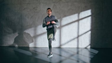 Boş bir çatı katında dizlerini esneten sportif bir adam. Kas sporcusu ayaklarını ısıtıyor spor salonunda antrenman yapmaya hazırlanıyor. Çekici esmer adam tek bacağını içeride egzersiz yapıyor. Spor konsepti 