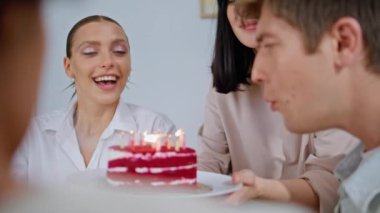 Ev partisinde gülümseyen adama doğum günü pastası getiren arkadaşlar. Heyecanlı adam arkadaşlarıyla mum üflüyor. Gülen dostlar, mutlu hissediyorlar dairede sevinçle 