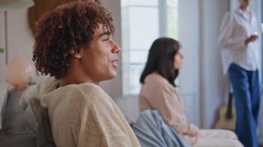 Yakın çekim kıvırcık adam oturma odasında arkadaşlarıyla iletişim kuruyor. Koltuğunda oturan çeşitli gençler rahat bir dairede birlikte takılıyorlar. Gülümseyen Latin delikanlılar evde dostça konuşuyorlar. İnsan yaşam tarzı