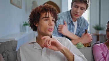 Yakın arkadaşlar ev partisinden bahsediyor. Hafif oturma odasında bira şişesi tutan genç adam iletişim arkadaşı. Kıvırcık genç adam evde el hareketleriyle konuşuyor. Parti gençleri eğleniyor.