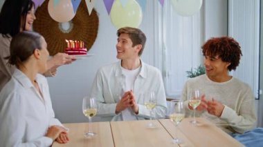 Arkadaşları sürpriz doğum günü çocuğu şirin pastayı yakın plan getiriyor. Kutlamada mum üfleyen mutlu adam dostça el çırpıyor. Gülümseyen gençler heyecanlı meslektaşlarını tebrik ediyor. 