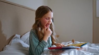 Tasasız bebek evde yumuşak yatağında oturup kitap izliyor. Sevimli küçük kız hafta sonunu dairede geçirmeye odaklanmış hissediyor. Makyajlı komik çocuk masal okuyor sayfaları tek başına çeviriyor 
