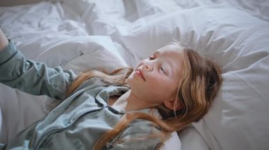 Pijamalı çocuk güneş ışığı yatak odasında tek başına yatıyor. Rahat çocuk yatakta güneşli tavşan taklidi yapıyor. Hafta sonu sabahı güneşi yansıtan küçük bir çocuk. Küçük kız kaygısız olmanın tadını çıkarıyor.