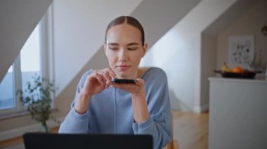 Sakin bir bayan sabah iş yerinde cep telefonuna göz atıyor. Tasasız kız akıllı telefon ekranında evde oturuyor. Beyaz iç mekanda cep telefonu tutan rahat bir kadın ev huzurunun tadını çıkarıyor. 