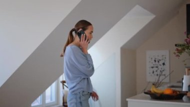 Rahat bayan ev mutfağından cep telefonunu arıyor. Modern dairede cep telefonuyla iletişim kuran mavi tişörtlü güzel bir kadın. Akıllı telefondan konuşan sakin bir kız, rahat bir ruh hali içinde.