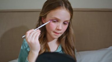 Komik çocuk, annesinin makyajlı yüzünü göz farı ile boyuyor. Mutlu bebek, elinde fırça tutan annenin kozmetik ürünleriyle deney yapıyor. Küçük kız yatak odasında tek başına eğleniyor. 
