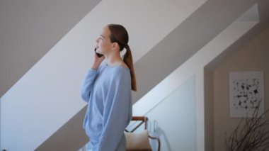 Oturma odasında akıllı telefondan konuşan düşünceli bir kız. Genç bayan cep telefonu sohbetini tavan arası penceresine bakarak yapıyor. Sakin bir kadın cep telefonunu arıyor. 
