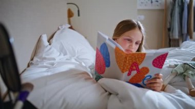 Odaklanmış çocuk kitap okuyor, yatak odasında dinleniyor. Güzel küçük kız rahat bir yatakta uzanmış peri masalının tadını çıkarıyor. Makyajlı komik çocuk hafta sonunu sabahları sayfalar çevirerek geçiriyor. Çocukluk kavramı 