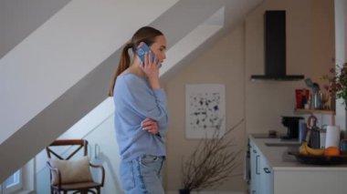Samimi bir dairede cep telefonuyla konuşan tasasız bir model. Rahatlamış genç bir bayan sabah akıllı telefonu arıyor. Nazik bir kadın telefonda konuşuyor. Tavan arasında rahat duruyor. Dostça iletişim konsepti 