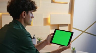 Yeşil ekran tabletindeki video içeriğini tarayan Freelancer uzak bir iş yerinde kapalı duruyor. Ofiste elinde krom anahtar bilgisayarı tutan bir adam. Mockup Gadget 'ta ciddi girişimci tarama raporu.