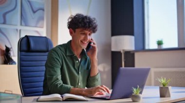 Pozitif çalışan konuşuyor, cep telefonu şirket masasında oturuyor, yakın plan. Gülümseyen adam, cep telefonu sohbetinin keyfini çıkar. Neşeli kıvırcık iş adamı akıllı telefonu arıyor..