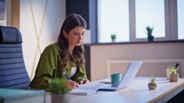 Şirket çalışanı, not defterine bilgi kaydediyor. Ofis masasında dizüstü bilgisayar aranıyor. Ciddi bir iş kadını defterine not alıyor. İşyerindeki bilgisayarda çalışan zarif bayan yönetici..