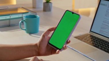 Ofiste el ele tutuşan yeşil ekran akıllı telefon. Yakın plan. İş yerinde dizüstü bilgisayarla Chroma Key cep telefonunu izleyen tanınmayan bir kadın. Modern evdeki iş kadını model cep telefonu arıyor..