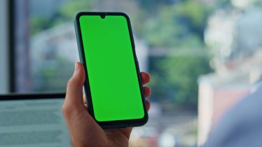 İş yerinde el ele tutuşan bir akıllı telefon. Yakın plan. Meçhul işadamı, modern ofisteki yeşil ekranlı cep telefonuyla sosyal medyayı tarıyor. Krom tuşlu cep telefonundan Freelancer mesajı okuyor.