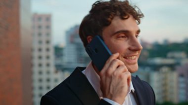 Ofis balkonunda akıllı telefondan konuşan zengin bir işadamı. Şehir manzaralı terasta cep telefonunu arayan kendinden emin bir adamın portresi. Başarılı patron açık havada cep telefonuyla pazarlık yapıyor..