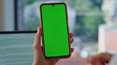 Modern ofis kapanışında parmaklar hareketli cep telefonu. Kimliği belirsiz bir kadın yeşil ekranlı cep telefonundan online uygulama satın alıyor. İş kadını iş yerinde krom anahtarlı akıllı telefon tutuyor.