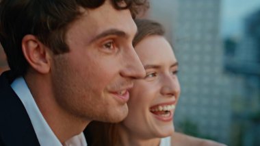 Yakından gülen çift şehir manzarasının tadını çıkarıyor çatıda romantik bir randevu. Sevgi dolu bir erkek ve kadın birlikte neşeli bir anı paylaşıyorlar. Şık kıyafetler içinde gülen eşler şehrin alaca karanlığına benziyor.