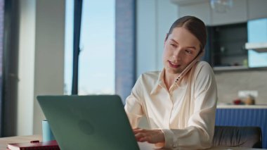 Ofiste cep telefonuyla konuşan profesyonel bir kadın dizüstü bilgisayarla yakın çekim yapıyor. Gülümseyen iş kadını çoklu görev çözme işini telefonla hallediyor. Kurumsal iletişimle meşgul neşeli bir bayan..