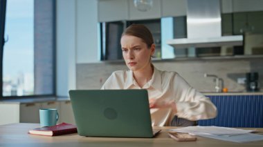 Ciddi iş kadını dizüstü bilgisayarla çalışıp ev mutfağını kapatmaya odaklandı. Aşırı çalışan kadın bilgisayarını kapatırken stres hissediyor. Yorgun kadın serbest çalışan uzak işyerindeki iş krizi yüzünden endişeli..
