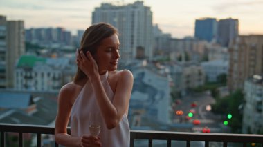 Rahat bayan teras restoranında dinleniyor sıcak bir akşamda şampanya tutuyor. Çatıdaki balkonda duran muhteşem kadın şehir manzarasını seyrediyor. Zarif elbiseli esmer şehir manzarasının tadını çıkarıyor.