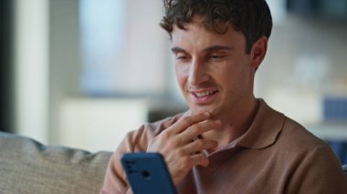 Kanepe modern apartman dairesinde neşeli ve akıllı bir adam. Gülümseyen adam ev ortamında cep telefonuyla mesajlaşıp hafta sonunun keyfini çıkarıyor. Yakışıklı esmer internetten cep telefonu kullanıyor.