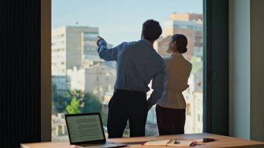 Pencere ofis binasını birlikte arayan şirket arkadaşları. Modern işyerindeki kadın çalışana şehir manzarası gösteren bir adam. İki başarılı iş ortağı içeride dostça sohbet ediyor.
