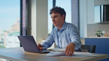 Merkezdeki bilgisayarın bilgisayarını inceleyen odaklanmış işadamı. Mutfaktaki bilgisayarı inceleyen ciddi bir adam. Modern işyerinde kahve içmekle meşgul bir erkek profesyonel.