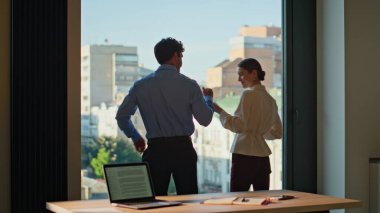 İş arkadaşı kadın, düşünceli, ofisteki panoramik pencereye kahve getiriyor. Dost canlısı erkek iş arkadaşı, şehir manzarasını iş kadınına göstermek için içecek kupası alıyor. İki ortak kapalı alanda mola veriyor.