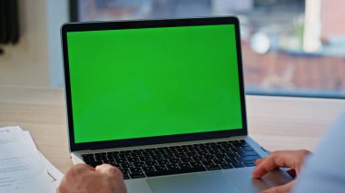 Yeşil ekran dizüstü bilgisayarı izleyen serbest çalışan iş belgeleriyle birlikte uzak bir yerde oturuyor. Kimliği belirsiz bir çalışan krom anahtar bilgisayarda giyiniyor. Model dijital aygıtında çalışan işadamı.